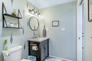 A bathroom with a toilet, sink, and shelves with decorative items.