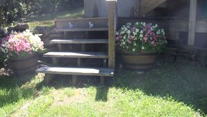 Een houten trap die leidt naar een gebouw, voorzien van een houten leuning. Aan beide zijden van de trap staan twee grote bloempotten met roze en witte bloemen.