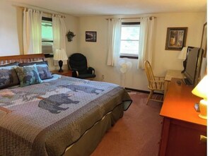 A hotel room with a bed, a desk, a chair, a TV, and two windows with curtains. - Waterfront property on pond with private dock . (Sunapee)
