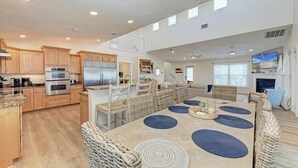 A spacious kitchen with modern appliances, a dining area with wicker chairs and blue placemats, and a living room with a fireplace and television. - 360* Views at "LGI Paradise" ~ Screened Porch w/ Hot Tub, Golf Cart included (Placida)