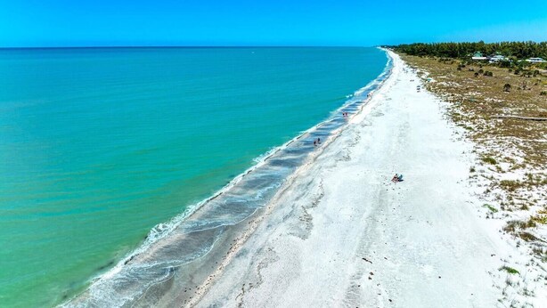 A beach with clear turquoise water, a sandy shore, and a line of trees in the background. - 360* Views at "LGI Paradise" ~ Screened Porch w/ Hot Tub, Golf Cart included (Placida)