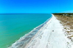 A beach with clear turquoise water, a sandy shore, and a line of trees in the background.