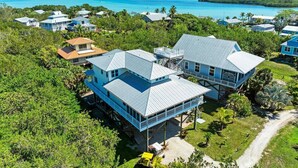 A large, multi-story house with a prominent balcony, surrounded by lush greenery and a view of the ocean. - 360* Views at "LGI Paradise" ~ Screened Porch w/ Hot Tub, Golf Cart included (Placida)