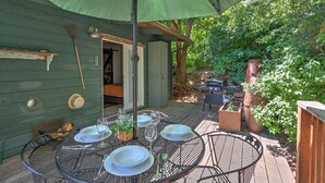 An outdoor patio with a table set for dining, surrounded by greenery and a wooden deck.