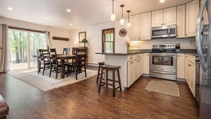 Una cocina con armarios de madera, microondas, horno y refrigerador. Hay una mesa de comedor con sillas y un taburete de bar.