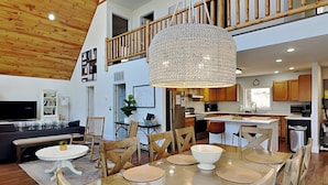 A spacious living area with a high ceiling, a dining table with chairs, a sofa, and a television. - Bearadise Found by Taylor Made Deep Creek (Swanton)