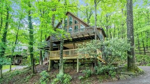 A cabin with a wooden deck and multiple levels, surrounded by dense forest. - Bearadise Found by Taylor Made Deep Creek (Swanton)