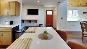 A modern kitchen with wooden cabinets, a built-in oven, and a dining area with a white table and chairs. - Bearadise Found by Taylor Made Deep Creek (Swanton)