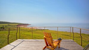 A wooden deck with a chair and binoculars, overlooking a beach and cliff. - 45 Steps - The Culinary Beachside Inn (Goose River)