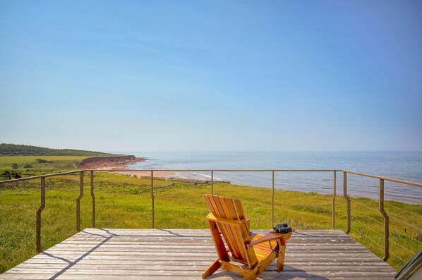 A wooden deck with a chair and binoculars, overlooking a beach and cliff. - 45 Steps - The Culinary Beachside Inn (Goose River)