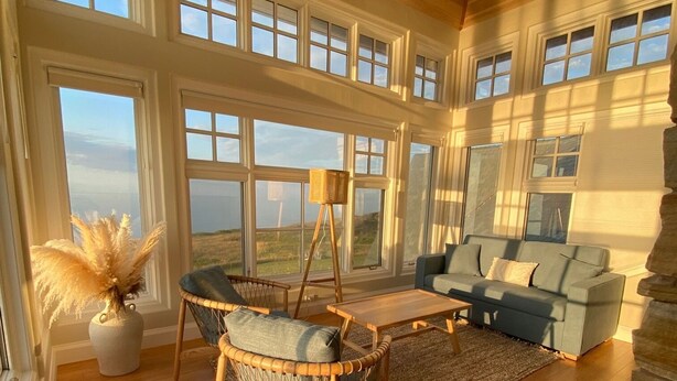 A spacious living room with large windows, a stone fireplace, and a view of the landscape. - 45 Steps - The Culinary Beachside Inn (Goose River)
