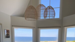A dining area with a view of the ocean, large windows, and wicker chairs. - 45 Steps - The Culinary Beachside Inn (Goose River)