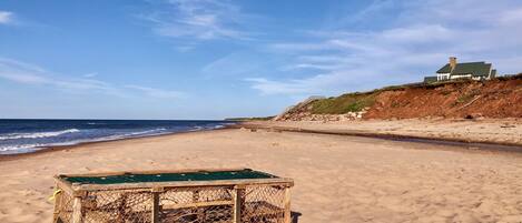 A beach with a wooden structure, a house on a cliff, and the ocean.