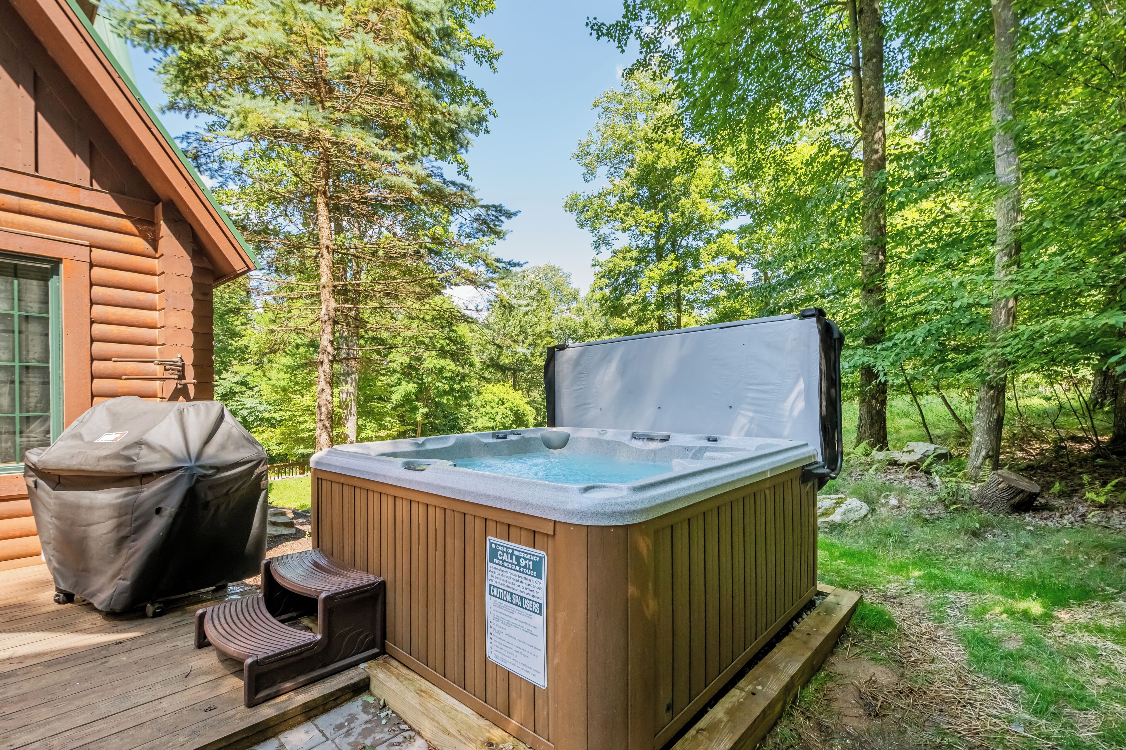 Un bain à remous sur une terrasse en bois, avec un panneau d’avertissement concernant la température élevée de l’eau.