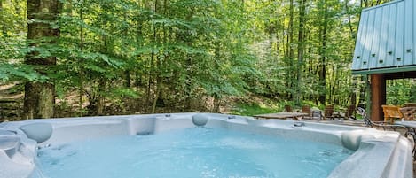 Un jacuzzi rodeado por un área boscosa con una terraza de madera y sillas.