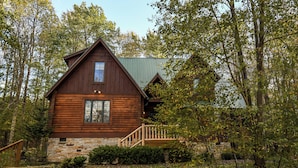 A log cabin with a stone foundation, a wooden deck, and a stone wall surrounding the property.