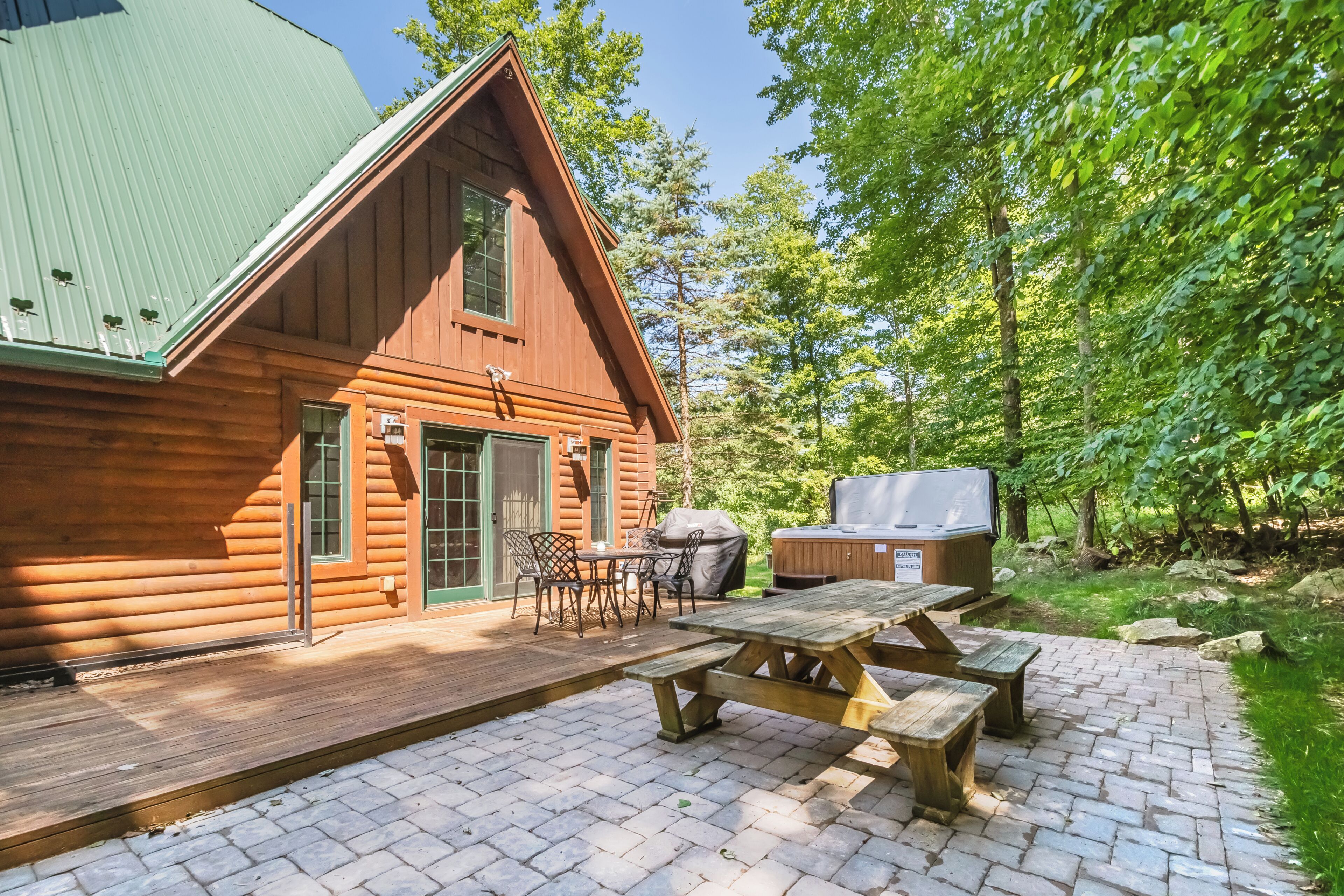 A wooden cabin with a deck, picnic table, and grill area.
