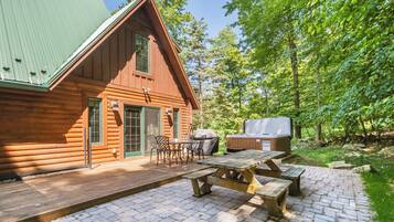 A wooden cabin with a deck, picnic table, and grill area.
