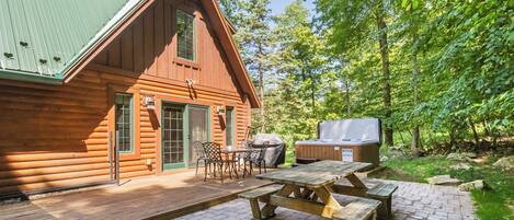A wooden cabin with a deck, picnic table, and grill area.