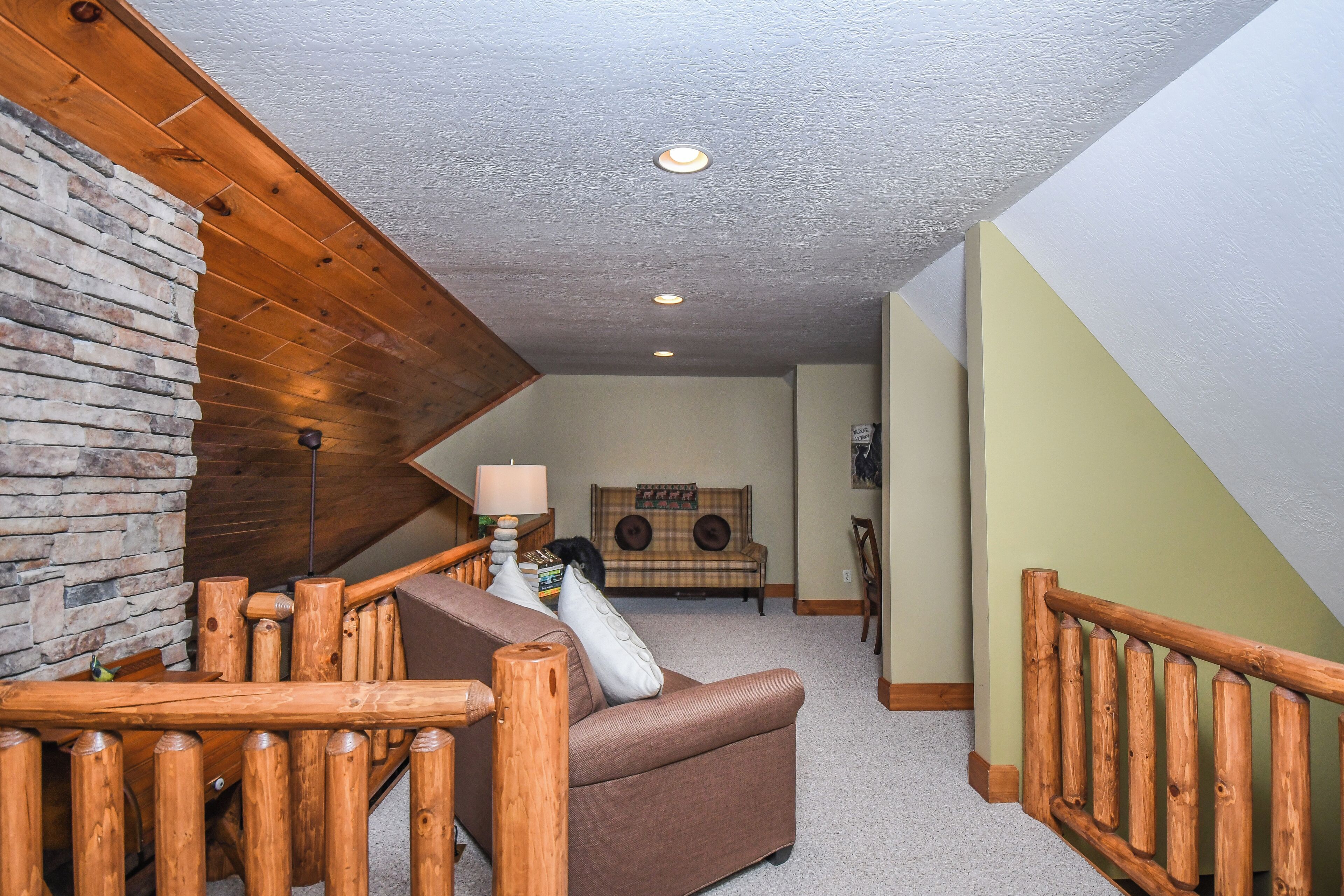 A cozy living area with a stone wall, wooden railing, and a brown sofa.