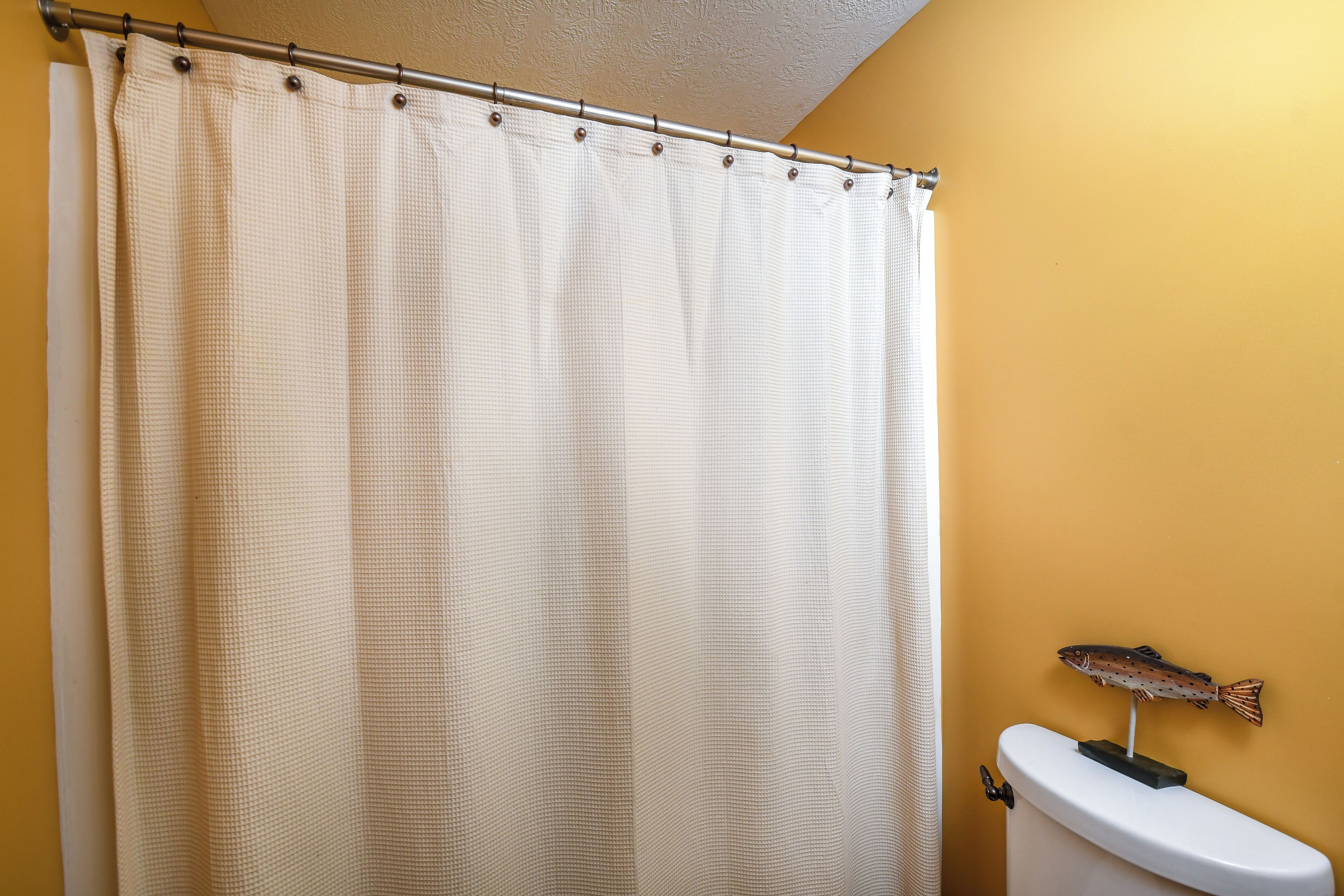 Une salle de bain avec un rideau de douche beige, des toilettes blanches et un motif décoratif représentant des poissons sur le mur.