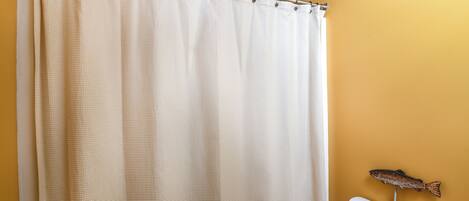 Une salle de bain avec un rideau de douche beige, des toilettes blanches et un motif décoratif représentant des poissons sur le mur.