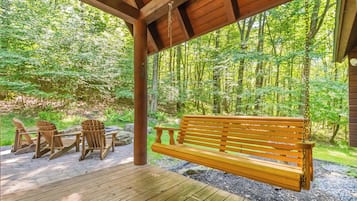 A wooden deck with a bench and Adirondack chairs, surrounded by a forest.