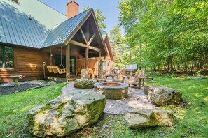 Une cabane rustique avec un toit en métal, un foyer en pierre et des meubles en bois, située dans une zone boisée.