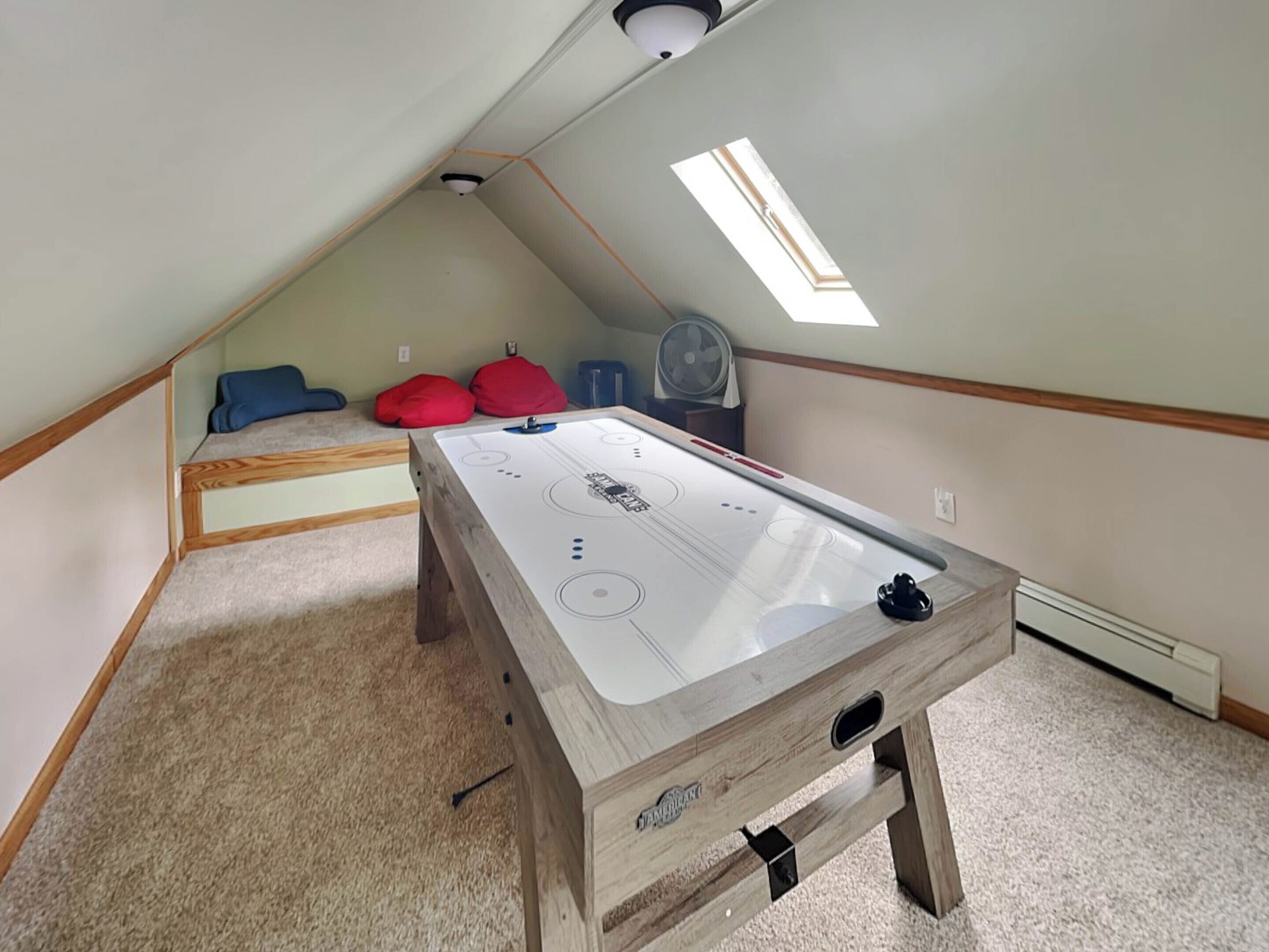 Een kleine kamer met een schuine kap, een tafelvoetbalspel, een ventilator en twee hippe zitzakken.