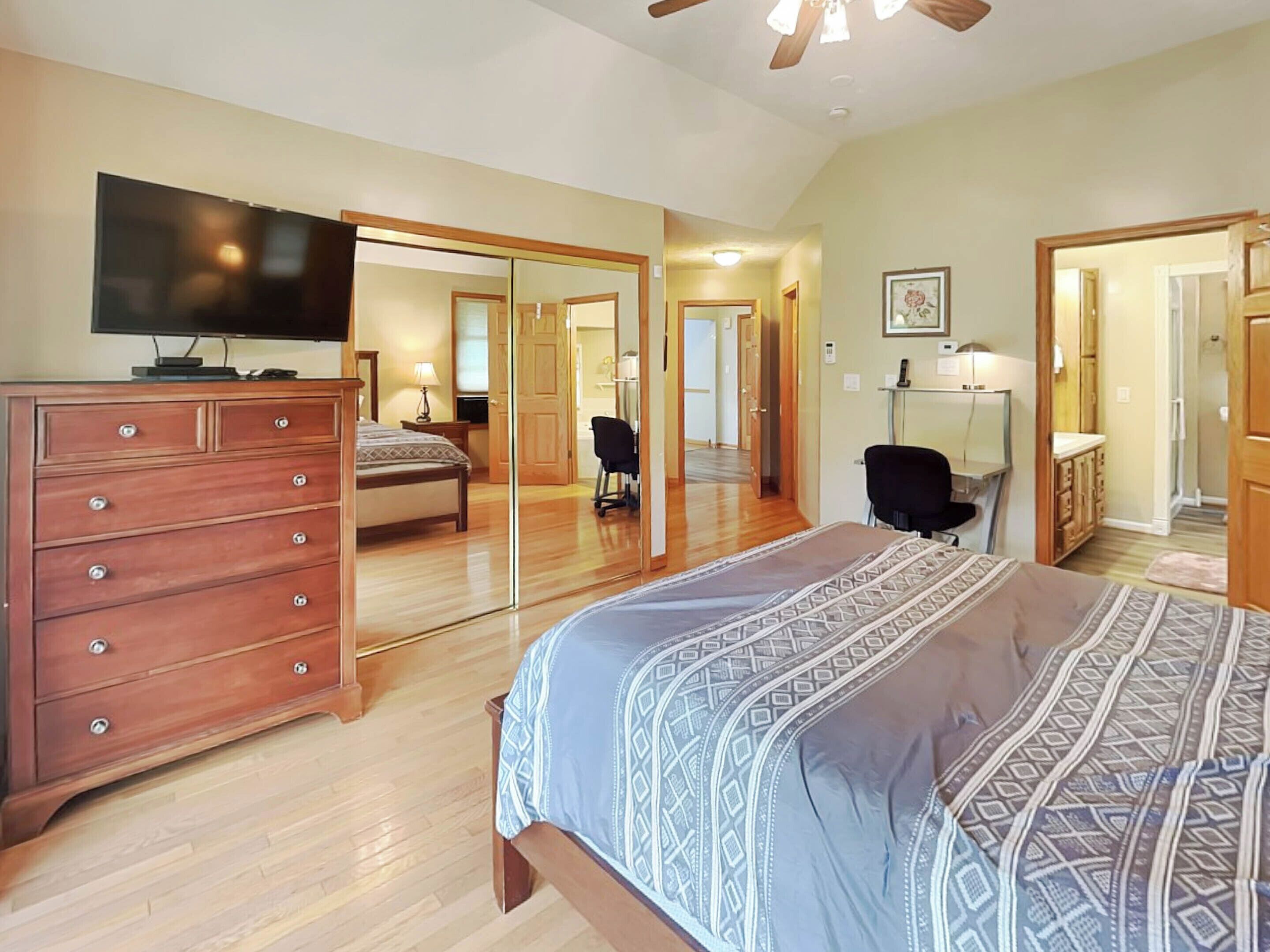 A bedroom with a bed, dresser, TV, and a large mirror.