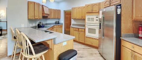 Una cocina moderna con armarios de madera, un refrigerador de acero inoxidable, un microondas y una encimera de granito.