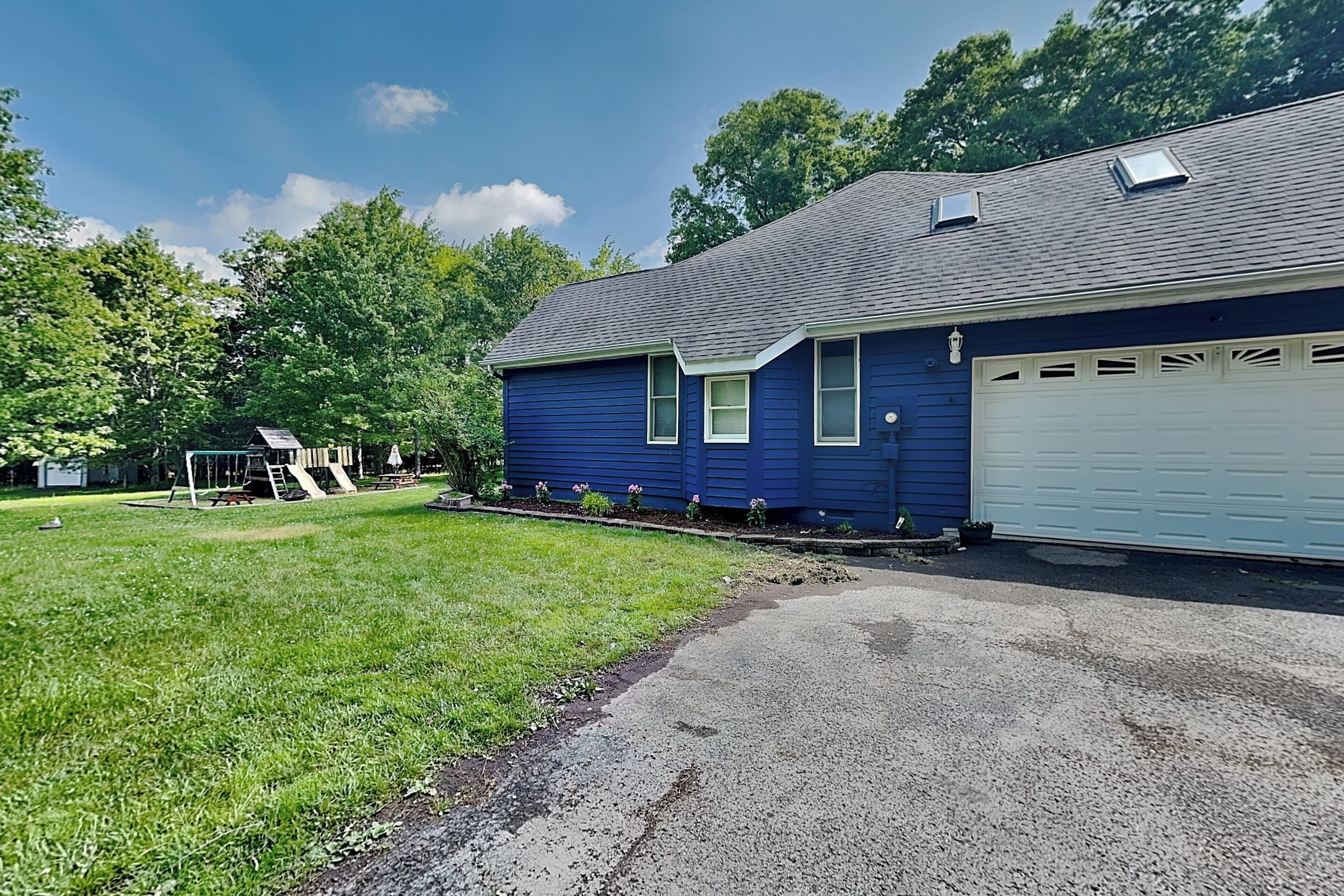 A two-story house with a garage, a well-maintained lawn, and a playground in the background.