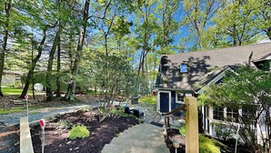 A wooden deck leading to a house with a stone pathway, surrounded by trees and a garden. - Bearfoot Lodge by Taylor Made Deep Creek (Oakland)