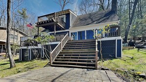 A two-story house with a wooden staircase leading to a balcony, surrounded by trees and a clear sky. - Bearfoot Lodge by Taylor Made Deep Creek (Oakland)