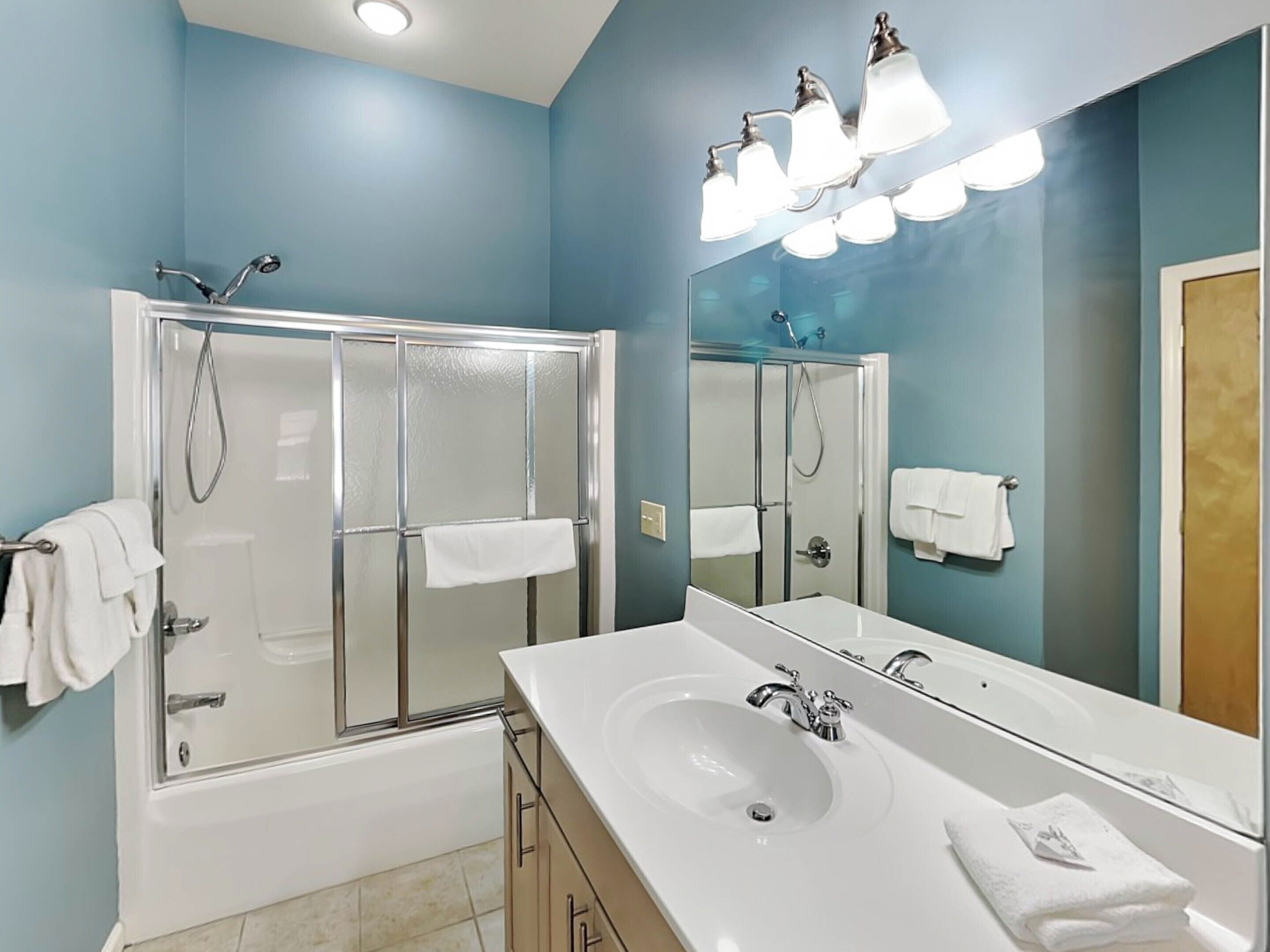 A bathroom with a glass-enclosed shower, a white sink, and a large mirror.