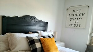 Una cama bien hecha con una variedad de almohadas y un letrero en la pared que dice "JUST ENOUGH grace for today".