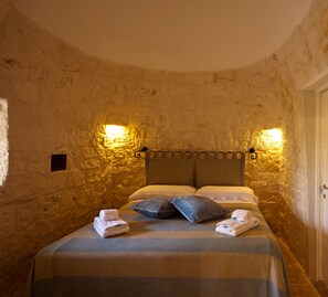 A stone-walled room with a bed, two pillows, and two folded towels.