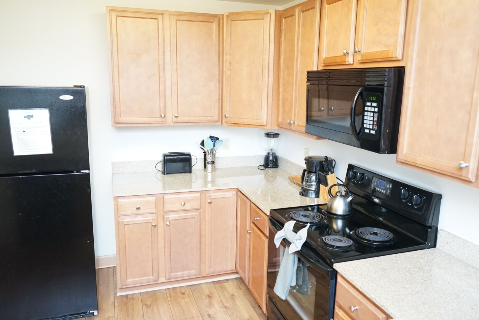 A kitchen with wooden cabinets, a black refrigerator, a microwave, a stove, and a toaster.