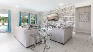 A modern living room with two grey sofas, a glass coffee table, and a TV mounted on a marble-patterned wall. - The Themepark Palace with Home Theater at Encore (Kissimmee)