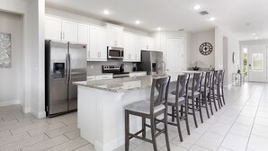 A modern kitchen with white cabinets, stainless steel appliances, and a central island with bar stools. - The Themepark Palace with Home Theater at Encore (Kissimmee)