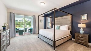 A bedroom with a four-poster bed, a nightstand with a lamp, a dresser, and a view of a patio with outdoor furniture. - The Themepark Palace with Home Theater at Encore (Kissimmee)