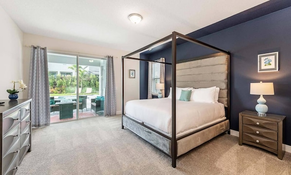 Quarto com uma cama de dossel, mesa de cabeceira com abajur, cômoda e vista para um pátio com mobiliário externo.