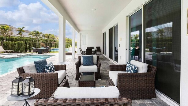 A covered outdoor seating area with wicker furniture, a pool, and a view of the surrounding landscape. - The Themepark Palace with Home Theater at Encore (Kissimmee)