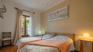 Ein Schlafzimmer mit zwei Betten, einem Fenster mit Vorhängen, einem Bild an der Wand und einem kleinen Tisch mit Lampe.