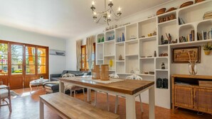 Ein geräumiges Wohnzimmer mit einer Holzbänken, einem Sofa und einem Esstisch. Weiße Regale mit verschiedenen Dekorationsobjekten und einer Deckenleuchte sind ebenfalls vorhanden.