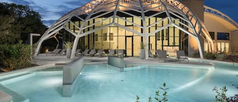 A modern hotel with a large outdoor pool, lounge chairs, and a unique arched glass structure.