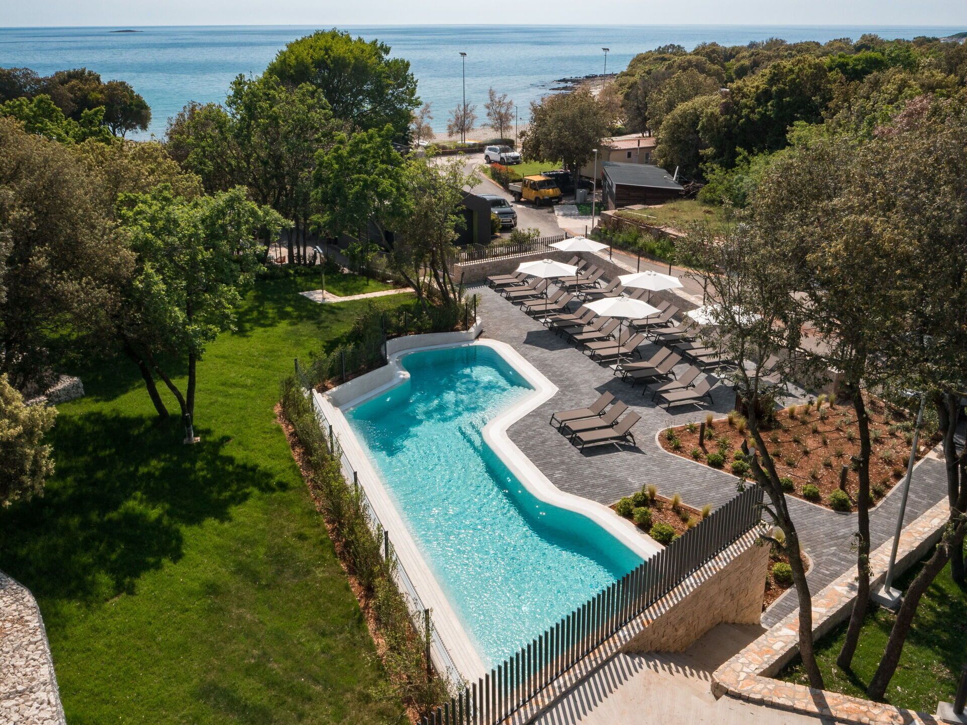 Une piscine à bord incurvé, entourée de chaises longues et de parasols, avec en arrière-plan des arbres et une vue sur la mer.