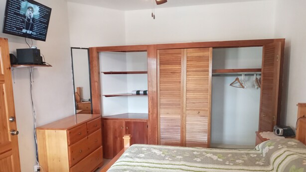 Ein Schlafzimmer mit einem Bett, einem Holzschrank, einem Fernseher und einem Schreibtisch.