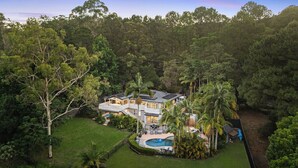 Una casa moderna rodeada de un bosque denso, con una amplia piscina y varias zonas de estar al aire libre.
