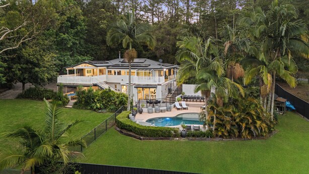 Una casa de dos pisos con piscina, rodeada de exuberante vegetación y palmeras.